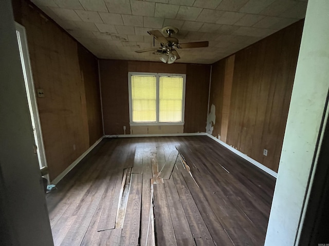 unfurnished room with ceiling fan, wood-type flooring, and wood walls