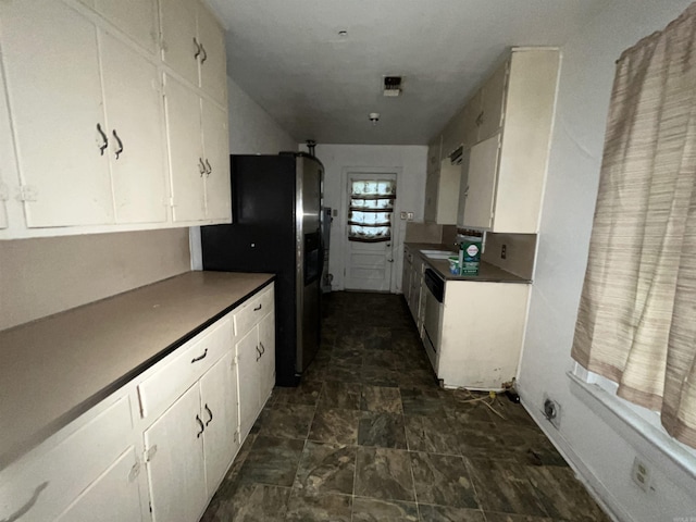 kitchen with appliances with stainless steel finishes, white cabinetry, and dark stone finish floors