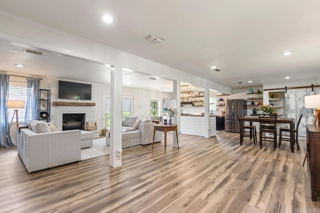 4 Coachlight Cir, Little Rock, AR 72227 - living area featuring a brick fireplace, wood finished floors, recessed lighting, crown molding, and a barn door