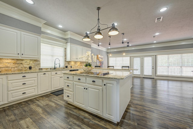 kitchen featuring a kitchen island, crown molding, black electric cooktop, white cabinets, and backsplash
