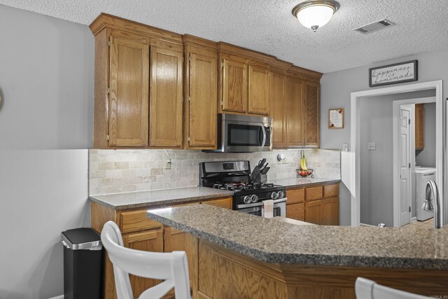 5132 Austin Lakes Cir, Sherwood, AR 72120 - kitchen featuring stainless steel appliances, a textured ceiling, brown cabinetry, and washer and dryer