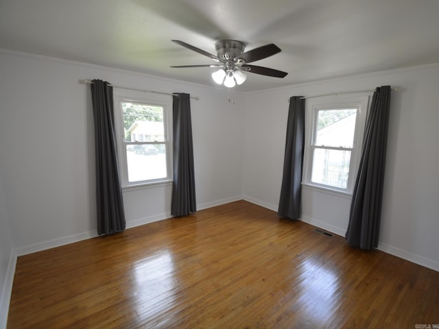empty room with healthy amount of natural light, wood finished floors, a ceiling fan, and crown molding