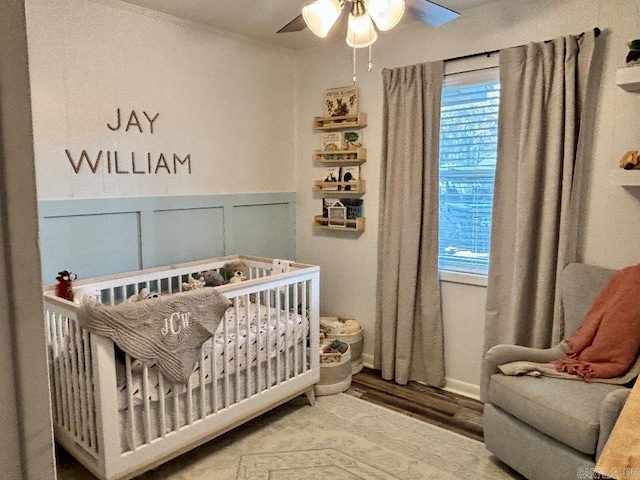 4 Paul St, Mcgehee, AR 71654 - bedroom with a nursery area, wood finished floors, ceiling fan, and a wainscoted wall
