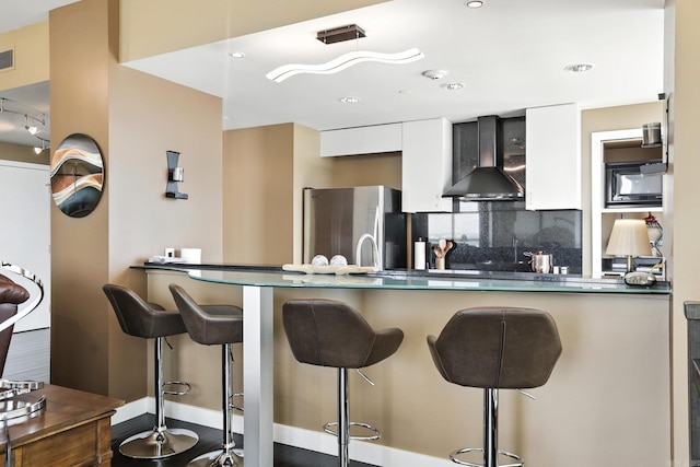 521 President Clinton Ave Unit 1101, Little Rock, AR 72201 - kitchen featuring wall chimney exhaust hood, freestanding refrigerator, white cabinetry, a kitchen bar, and recessed lighting