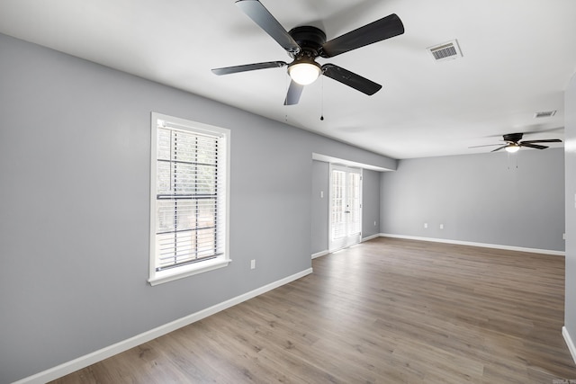empty room with a ceiling fan, healthy amount of natural light, and wood finished floors
