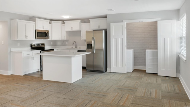 300 W Pleasure Ave, Searcy, AR 72143 - kitchen featuring appliances with stainless steel finishes, washing machine and clothes dryer, light colored carpet, white cabinetry, and a center island