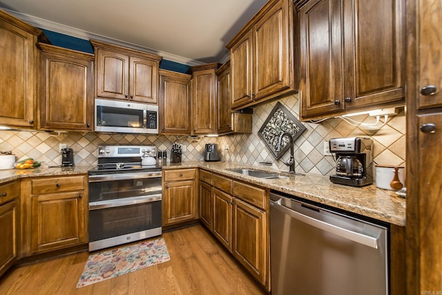 3200 Overcup Dr, Sherwood, AR 72120 - kitchen featuring appliances with stainless steel finishes, light stone counters, light wood-type flooring, decorative backsplash, and ornamental molding