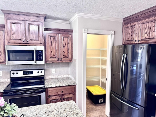 kitchen with stainless steel appliances, decorative backsplash, a textured ceiling, light stone countertops, and ornamental molding