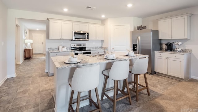 kitchen featuring appliances with stainless steel finishes, a kitchen breakfast bar, an island with sink, recessed lighting, and light stone counters