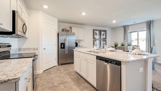 kitchen with stainless steel appliances, white cabinetry, an island with sink, light stone counters, and recessed lighting