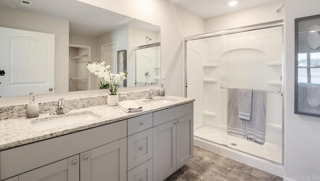 bathroom featuring a shower stall, double vanity, and a walk in closet
