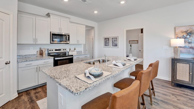3416 Hank Dr, Jonesboro, AR 72404 - kitchen featuring stainless steel appliances, dark wood-type flooring, a kitchen bar, an island with sink, and light stone countertops