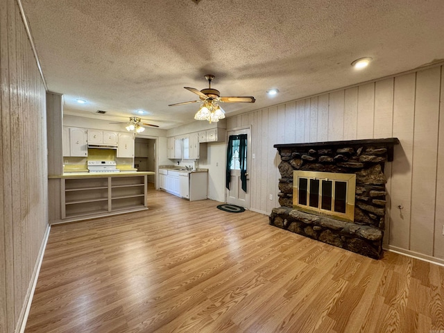 701 Emerald Gardens Dr, North Little Rock, AR 72118 - unfurnished living room with light wood-style flooring, a textured ceiling, a ceiling fan, a stone fireplace, and wood walls