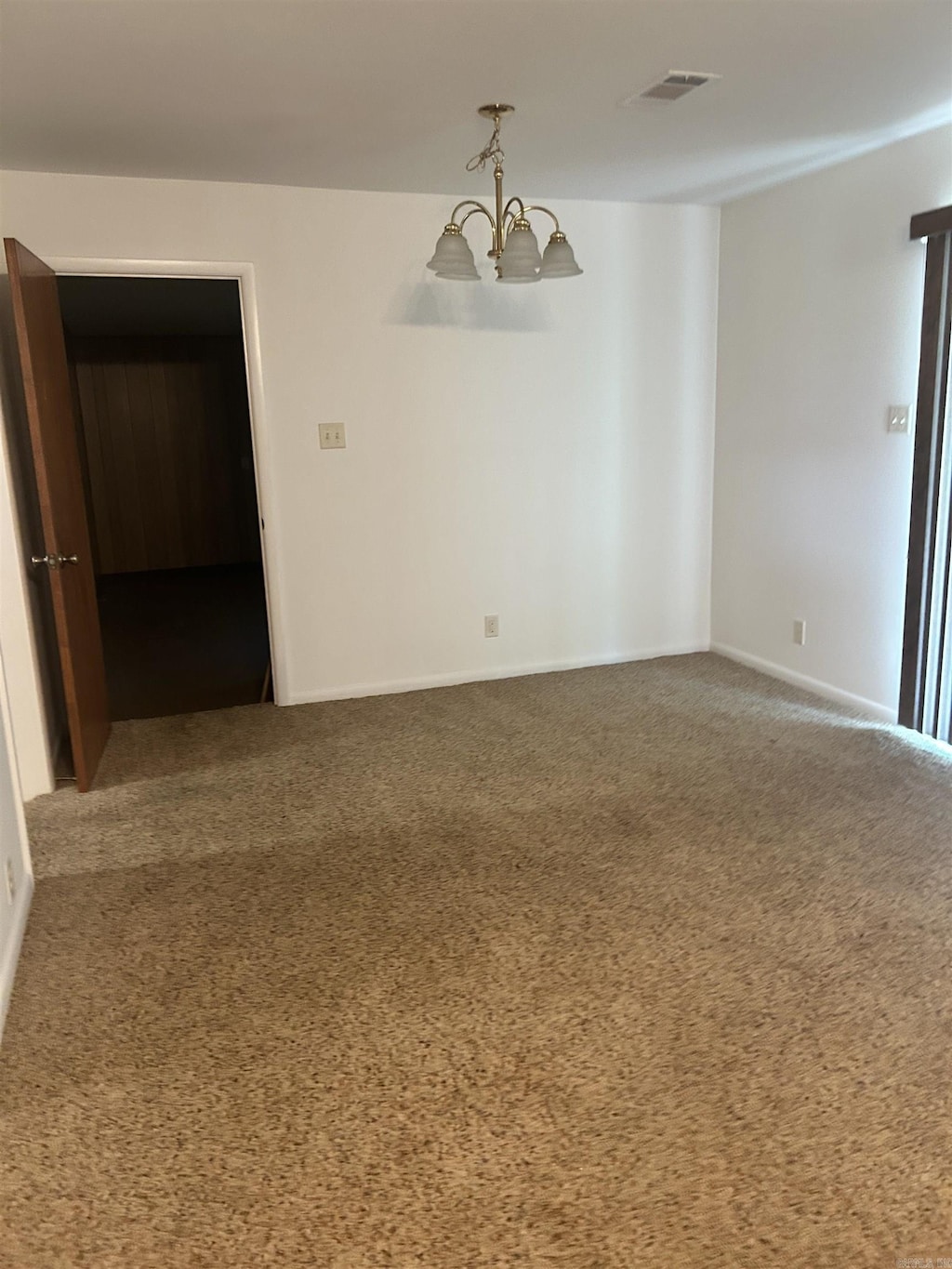 carpeted spare room with a chandelier and baseboards