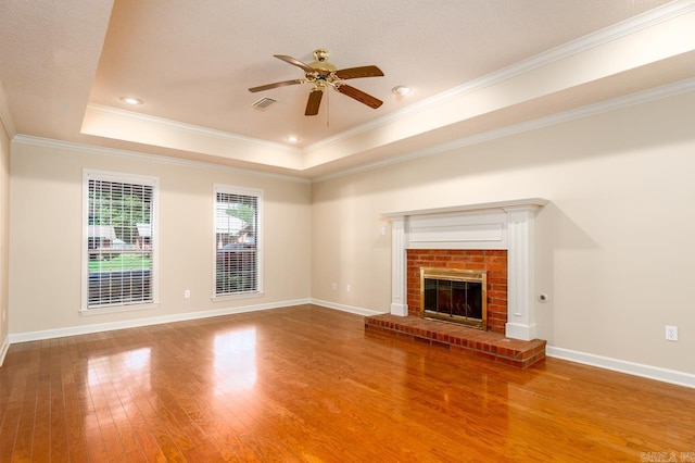 1940 Payne Ln, Conway, AR 72034 - unfurnished living room with wood-type flooring, a ceiling fan, a tray ceiling, ornamental molding, and a brick fireplace