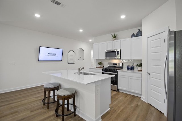 6804 Cypress Trl, North Little Rock, AR 72113 - kitchen featuring appliances with stainless steel finishes, a breakfast bar, white cabinets, backsplash, and wood finished floors