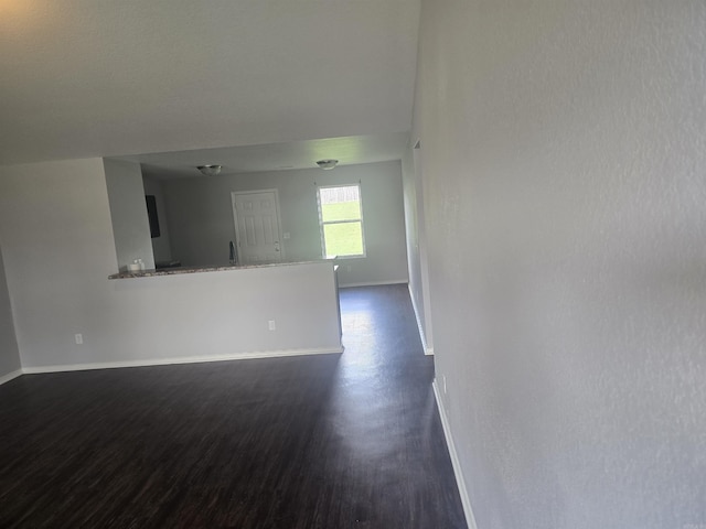 unfurnished living room featuring baseboards and dark wood-type flooring