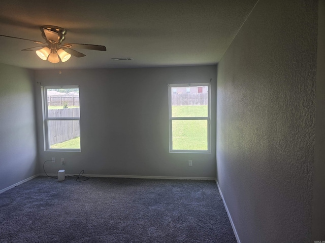 empty room featuring a textured wall, dark colored carpet, and a ceiling fan