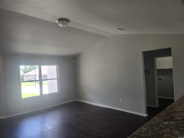 unfurnished room with a textured ceiling, vaulted ceiling, and dark wood-style floors