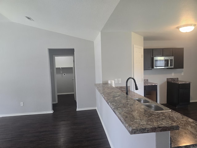 kitchen with stainless steel microwave, dark wood-style flooring, a peninsula, lofted ceiling, and dark countertops