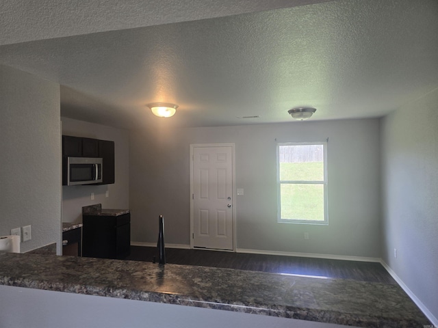 kitchen featuring stainless steel microwave, dark wood finished floors, a textured ceiling, and dark countertops