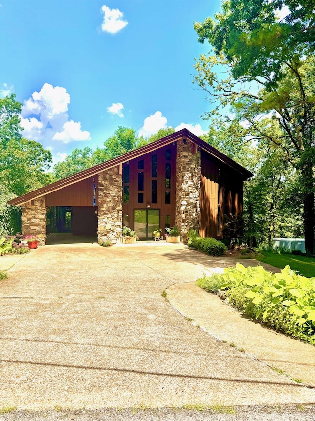 mid-century modern home featuring stone siding, concrete driveway, a carport, and board and batten siding