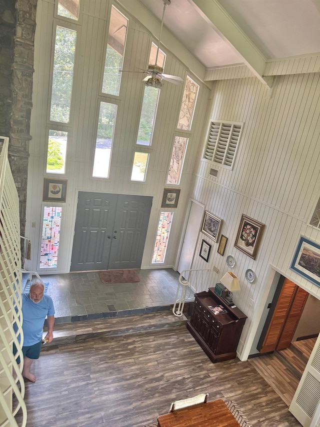 foyer entrance featuring wood finished floors, wood walls, a ceiling fan, and beamed ceiling