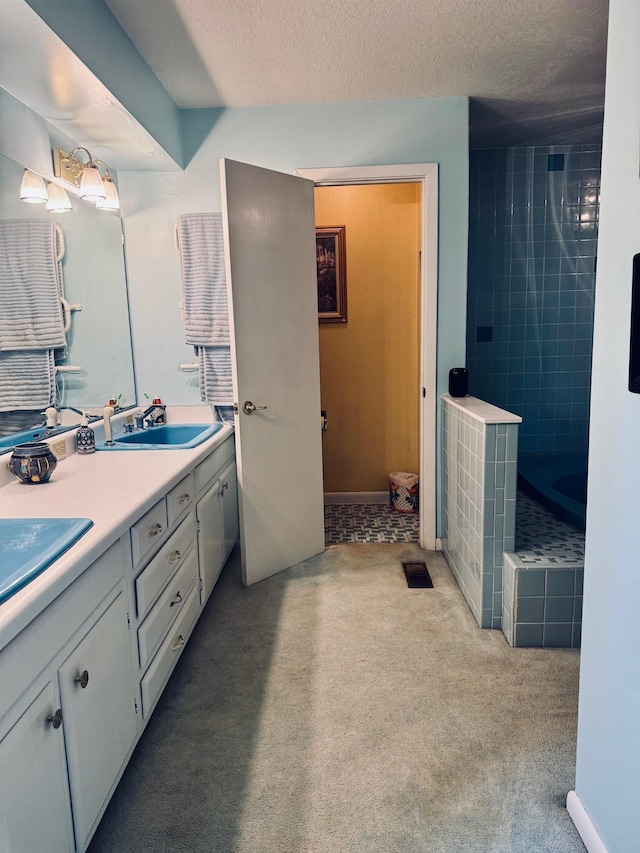full bath with double vanity, a tile shower, and a textured ceiling