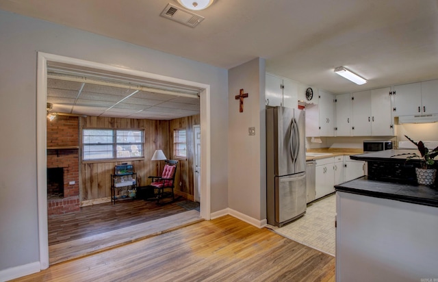 111 Greenland Cv, Little Rock, AR 72204 - kitchen featuring stainless steel appliances, light wood-type flooring, white cabinetry, a fireplace, and wood walls