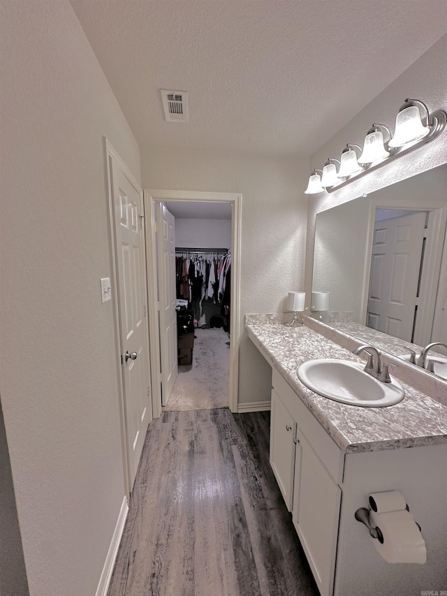 bathroom featuring vanity, wood finished floors, a walk in closet, and a textured ceiling