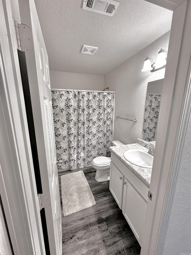 full bathroom featuring wood finished floors, vanity, a textured ceiling, a textured wall, and a shower with curtain