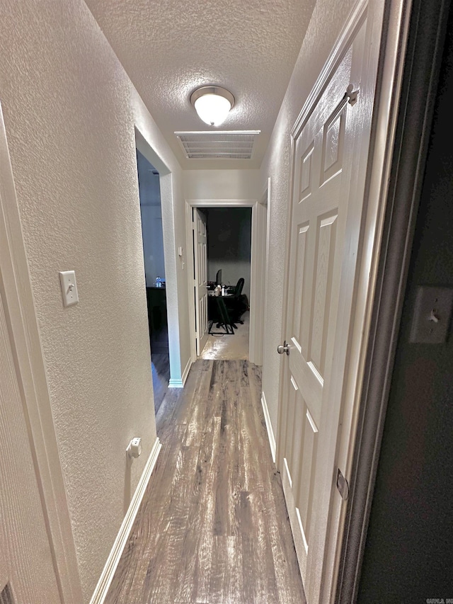 corridor with a textured ceiling, a textured wall, and wood finished floors
