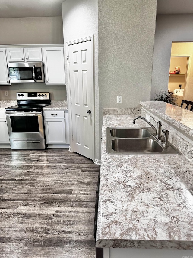 kitchen with appliances with stainless steel finishes, a textured wall, white cabinets, dark wood-style floors, and light countertops