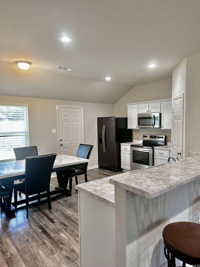 kitchen featuring appliances with stainless steel finishes, vaulted ceiling, dark wood-type flooring, light countertops, and white cabinetry