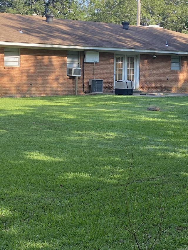 rear view of property featuring brick siding, a yard, cooling unit, and roof with shingles