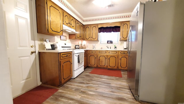 81 Pheasant Run Dr, Cabot, AR 72023 - kitchen featuring freestanding refrigerator, white range with gas stovetop, under cabinet range hood, brown cabinets, and light wood-style flooring