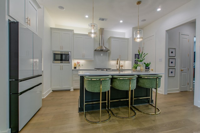 101 Mergeron Ct, Little Rock, AR 72212 - kitchen featuring freestanding refrigerator, stainless steel microwave, wall chimney exhaust hood, light wood-type flooring, and a center island with sink