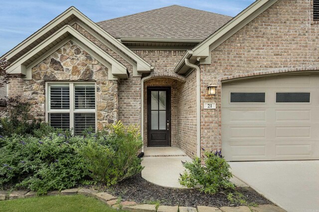 21 Piper Ln, Little Rock, AR 72223 - view of exterior entry with an attached garage, a shingled roof, brick siding, driveway, and stone siding