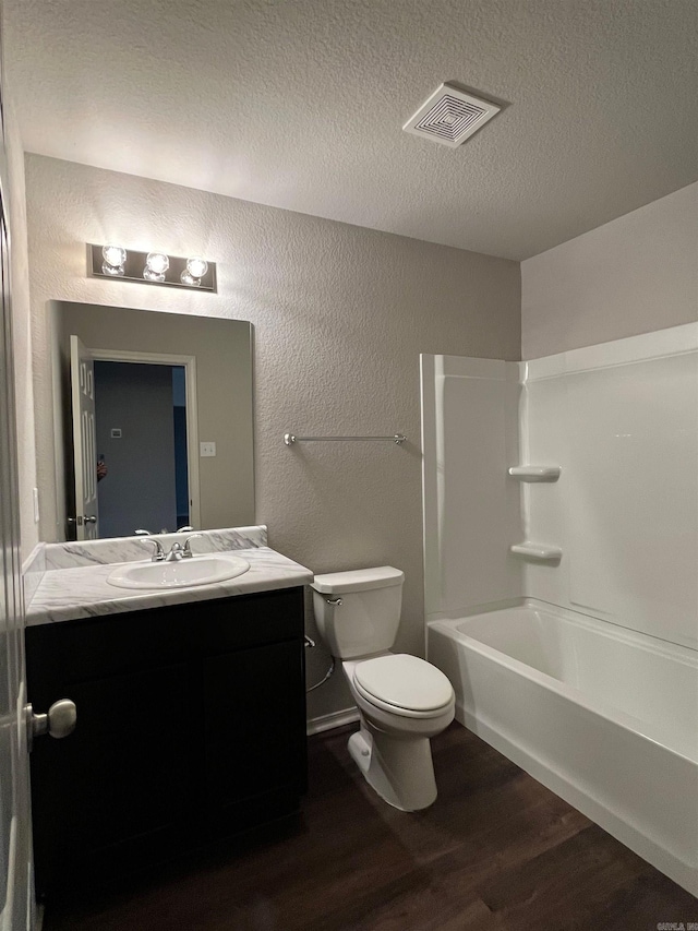 full bath featuring wood finished floors, vanity, a textured wall, a textured ceiling, and washtub / shower combination
