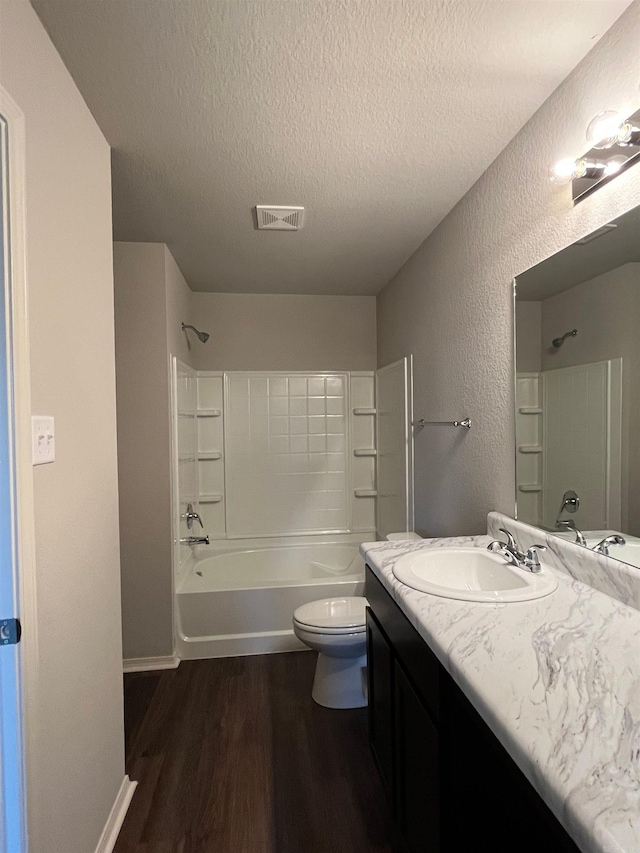 full bath featuring wood finished floors, a textured ceiling, vanity, a textured wall, and tub / shower combination