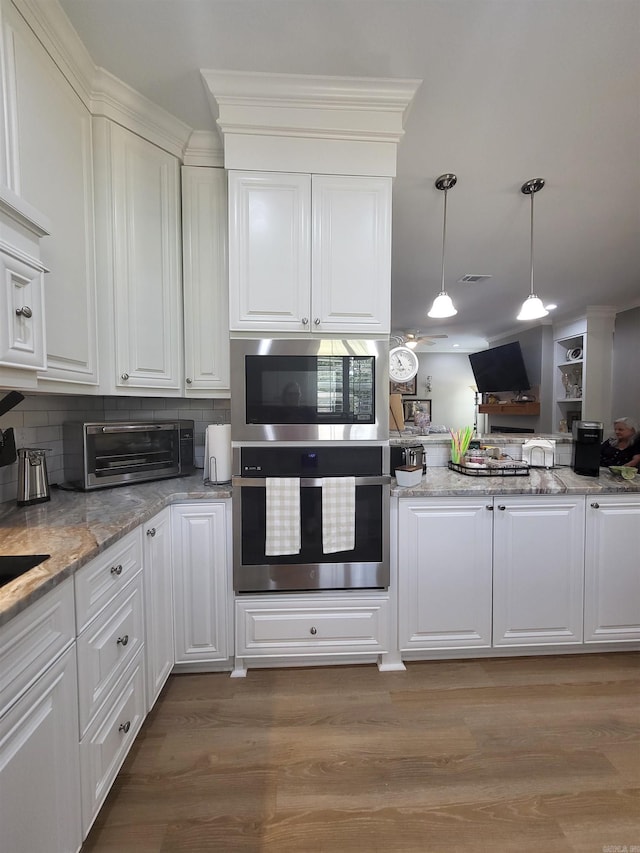 6413 Ram Rd, Mabelvale, AR 72103 - kitchen featuring stainless steel oven, built in microwave, light wood-type flooring, white cabinetry, and decorative light fixtures