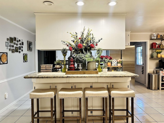 1912 W Arch Ave, Searcy, AR 72143 - kitchen featuring light tile patterned floors, a breakfast bar area, ornamental molding, white cabinets, and freestanding refrigerator
