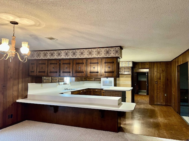 101 Fairway Dr, Bald Knob, AR 72010 - kitchen featuring wall oven, a chandelier, wooden walls, dark brown cabinets, and light countertops