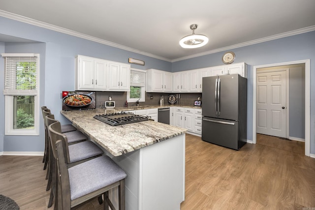 914 Cartier Ln, Little Rock, AR 72211 - kitchen with stainless steel appliances, a peninsula, white cabinetry, light stone counters, and light wood-style floors