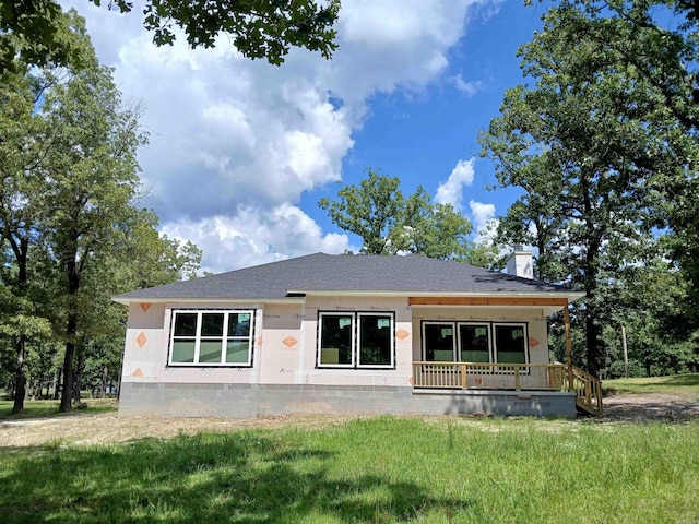rear view of property featuring covered porch, a lawn, and a chimney