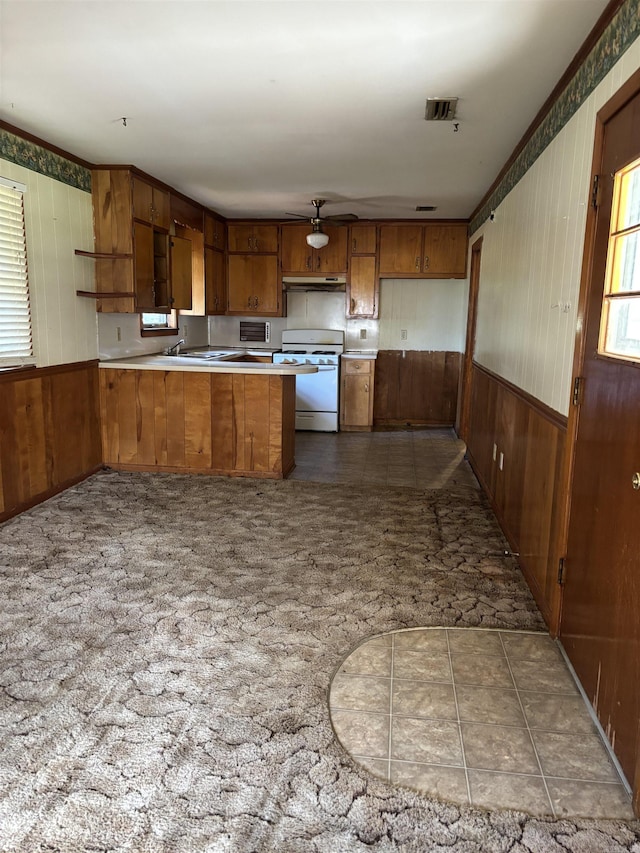 513 Joyce, Searcy, AR 72143 - kitchen featuring white gas range oven, brown cabinets, under cabinet range hood, a peninsula, and wooden walls