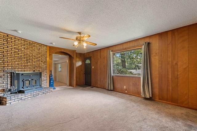 7025 Windsong, North Little Rock, AR 72113 - unfurnished living room featuring arched walkways, ceiling fan, carpet flooring, a wood stove, and a textured ceiling
