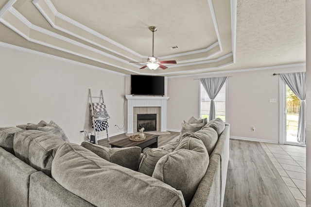 19 Mustang, Cabot, AR 72023 - living room featuring a raised ceiling, ceiling fan, crown molding, a tiled fireplace, and light wood-style floors