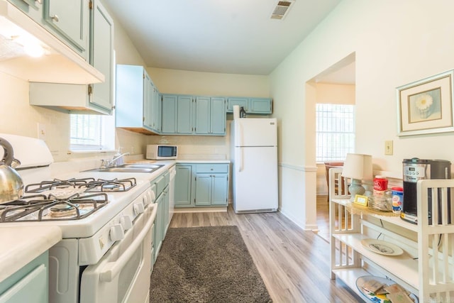 4624 W 29th St, Little Rock, AR 72204 - kitchen with white appliances, light wood-style flooring, under cabinet range hood, light countertops, and blue cabinetry