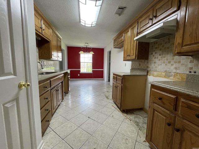 3806 Winterbrook Dr, Benton, AR 72015 - kitchen with brown cabinets, under cabinet range hood, tasteful backsplash, light tile patterned flooring, and a textured ceiling